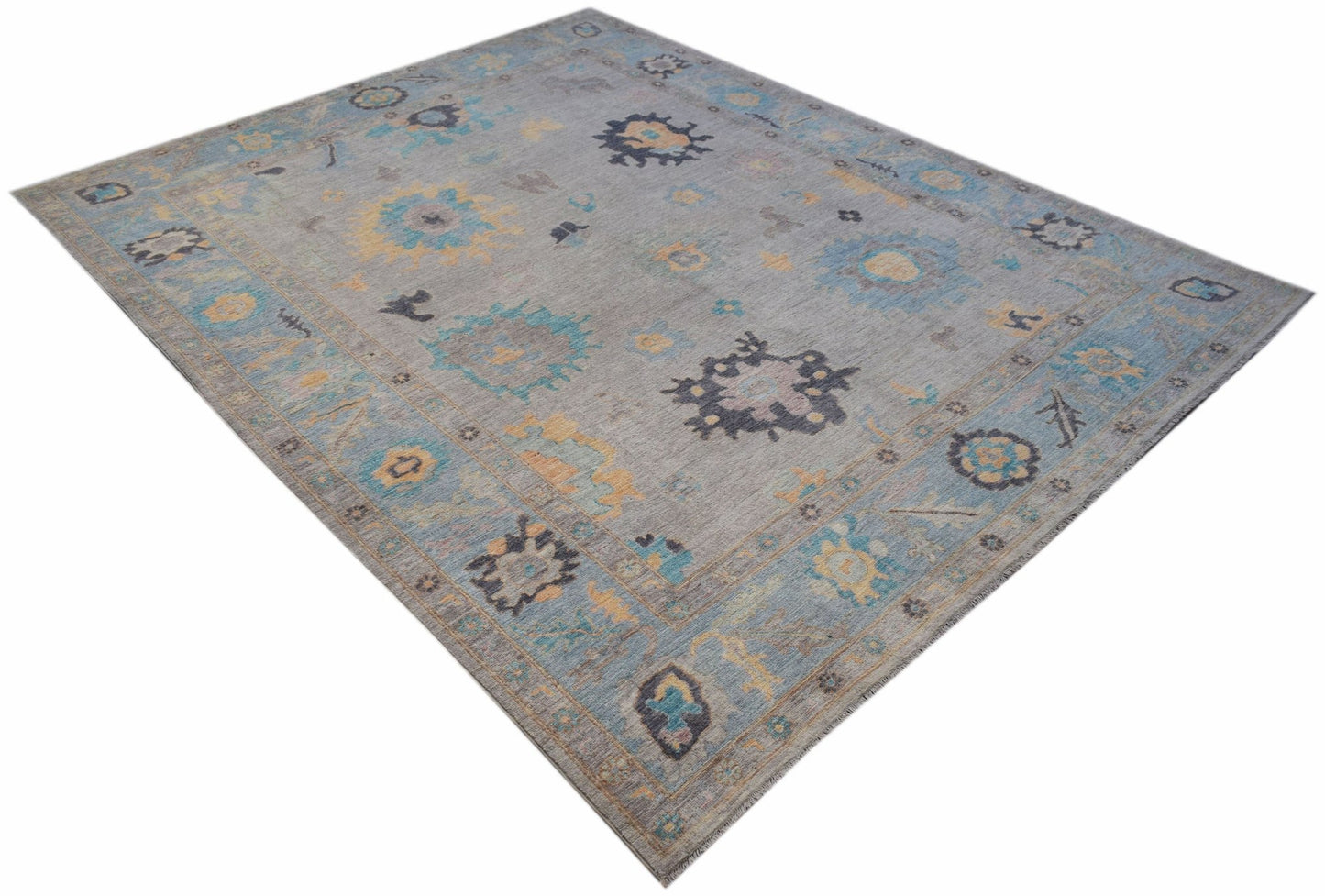 A handwoven transitional Oushak rug featuring a floral pattern in blue, yellow, and grey tones.