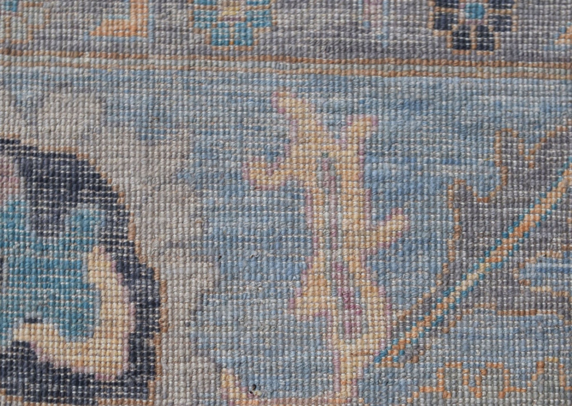 A close-up of a handwoven transitional Oushak rug featuring a blue floral pattern on wool.