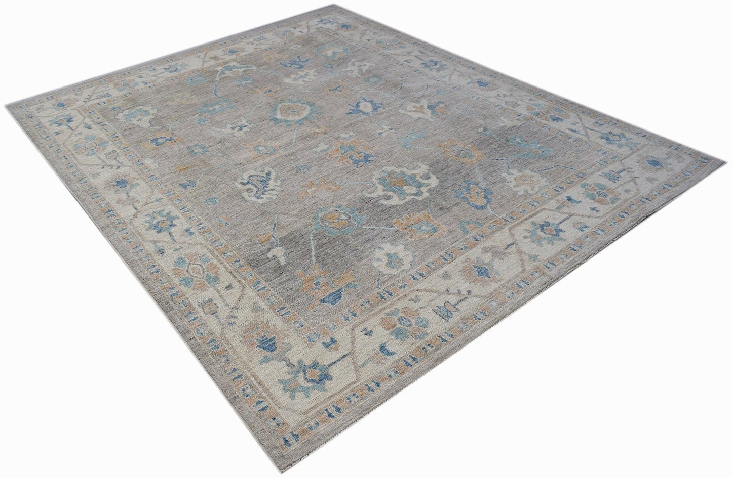 A handwoven transitional Oushak rug featuring a floral pattern in blue and tan on a grey field.