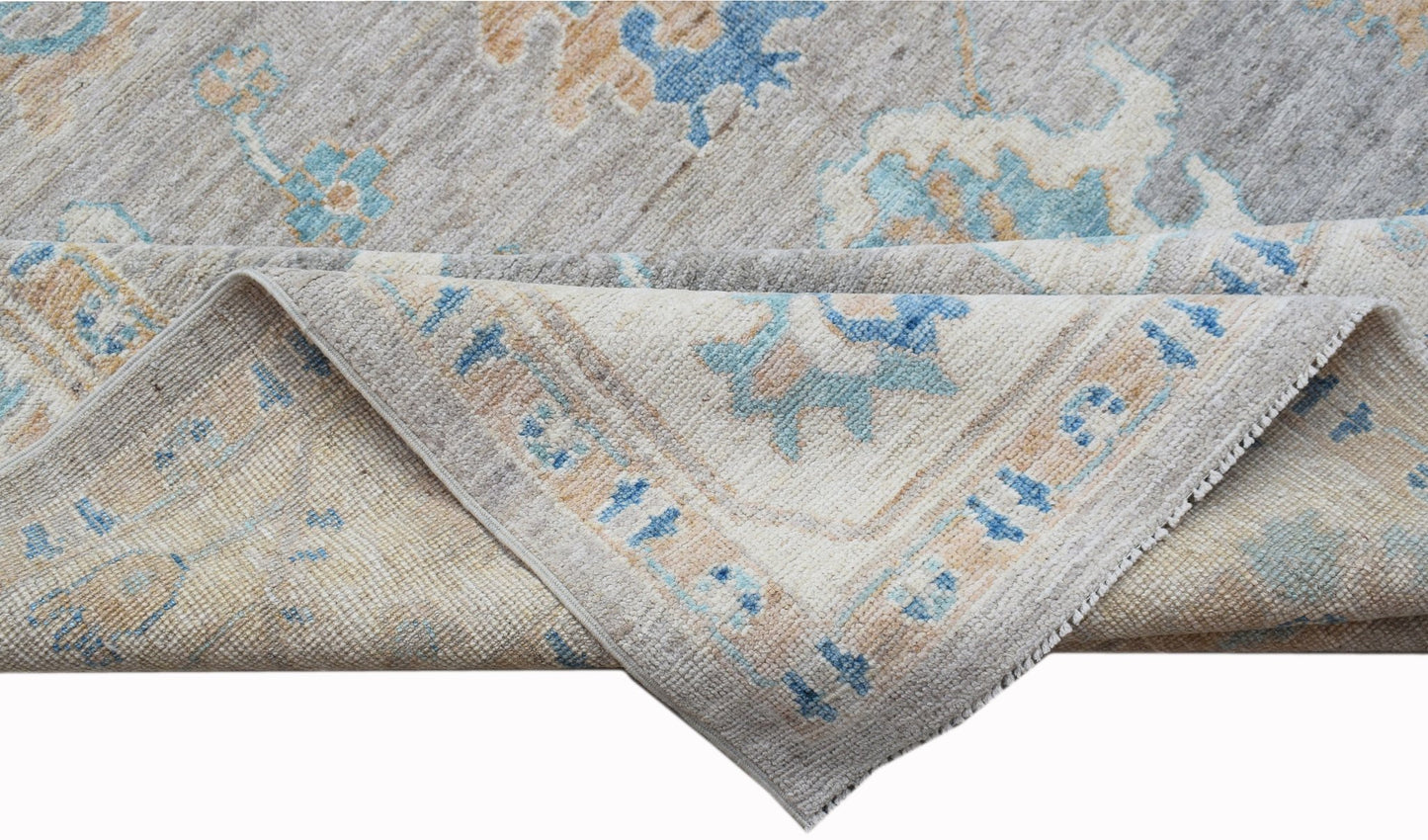 A handwoven transitional Oushak rug featuring a floral pattern in blue, beige, and grey tones.