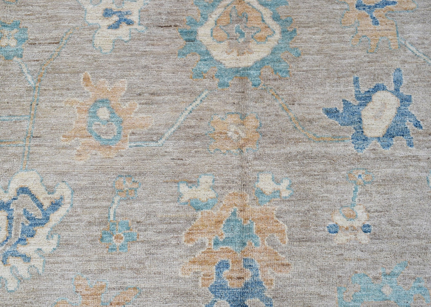 A handwoven transitional Oushak rug featuring a floral pattern in blue and tan on a grey field.