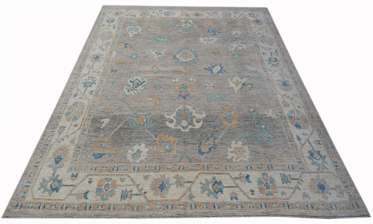 A handwoven transitional Oushak rug featuring a floral pattern in blue and tan on a grey field.