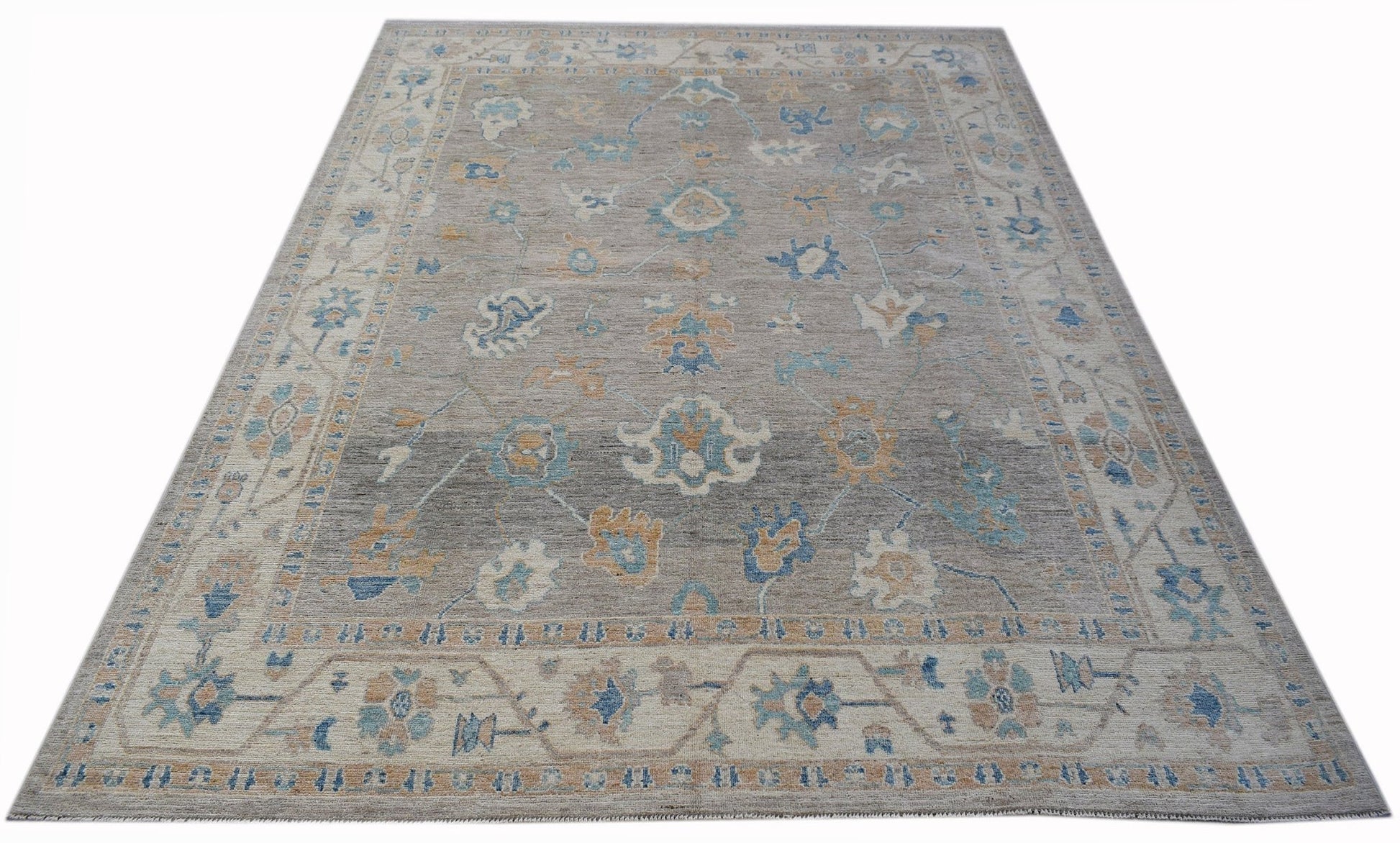 A handwoven transitional Oushak rug featuring a floral pattern in blue and tan on a grey field.