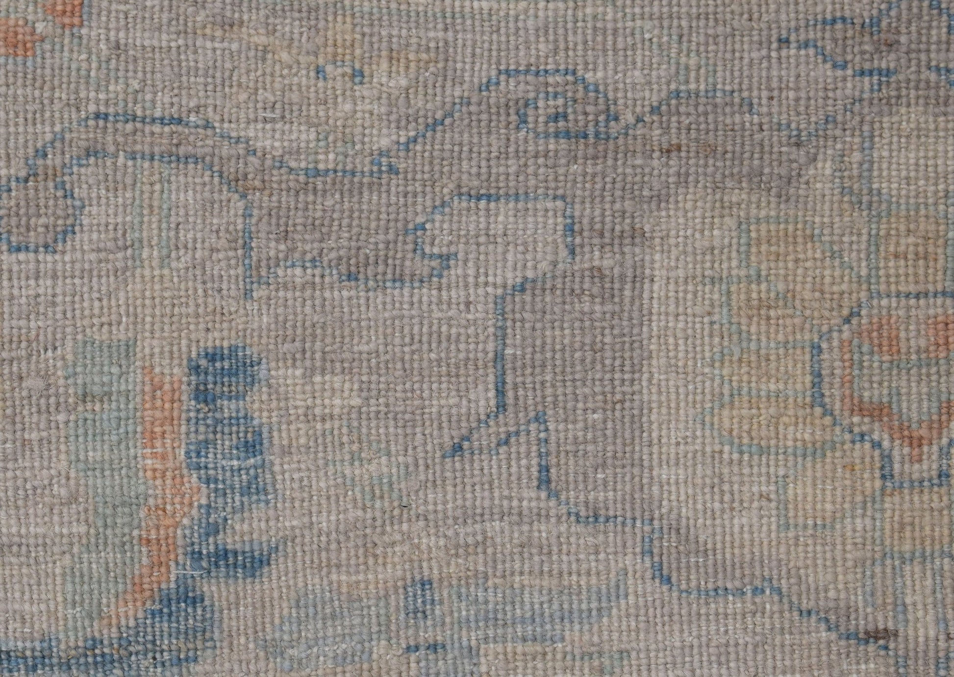 A close-up of a handwoven transitional Oushak rug featuring a faded floral pattern in blue and tan.