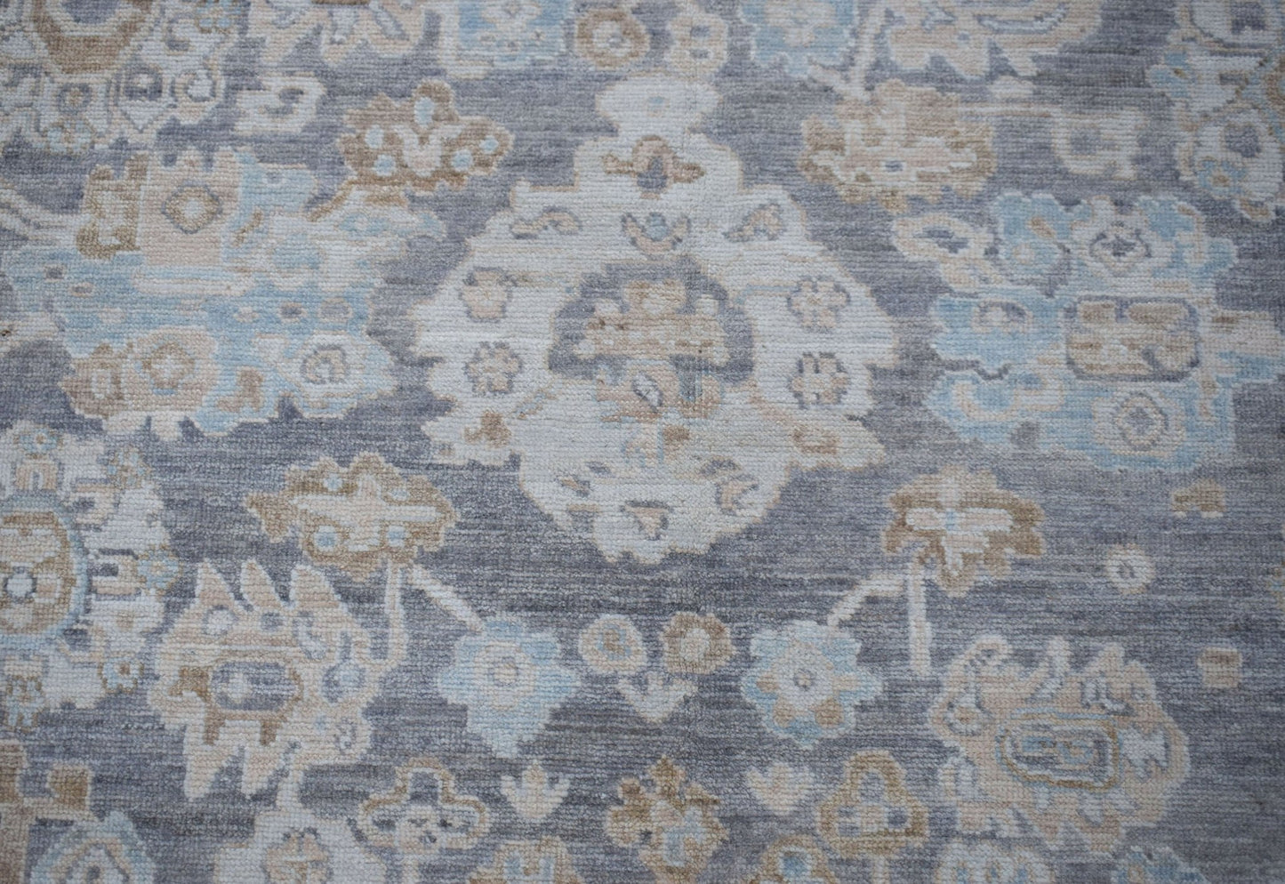 A handwoven transitional Oushak rug featuring a floral pattern in shades of grey, blue, and beige.