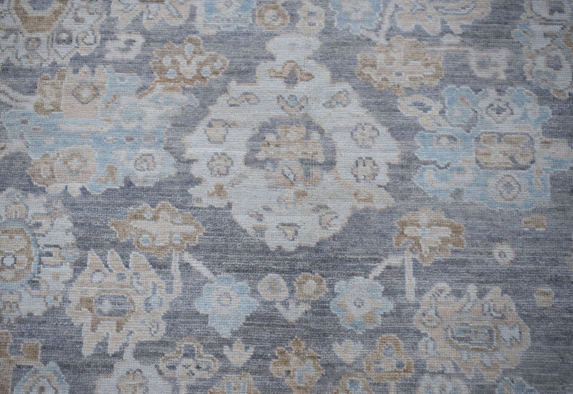 A handwoven transitional Oushak rug featuring a floral pattern in shades of grey, blue, and beige.
