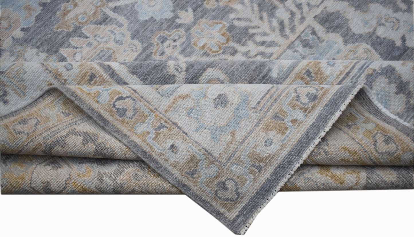 A handwoven transitional Oushak rug featuring a floral pattern in shades of grey, blue, and tan.