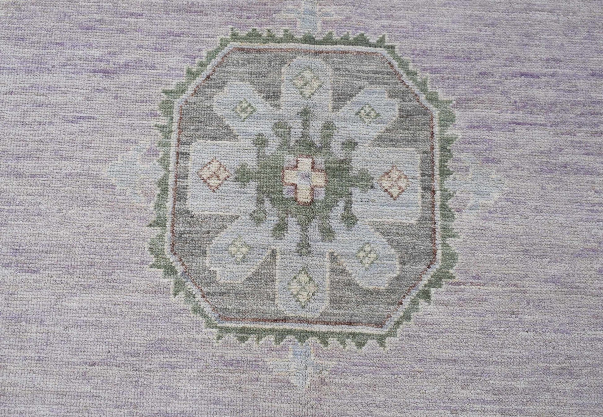 A handwoven transitional Oushak rug featuring a central floral medallion in soft lavender and grey.