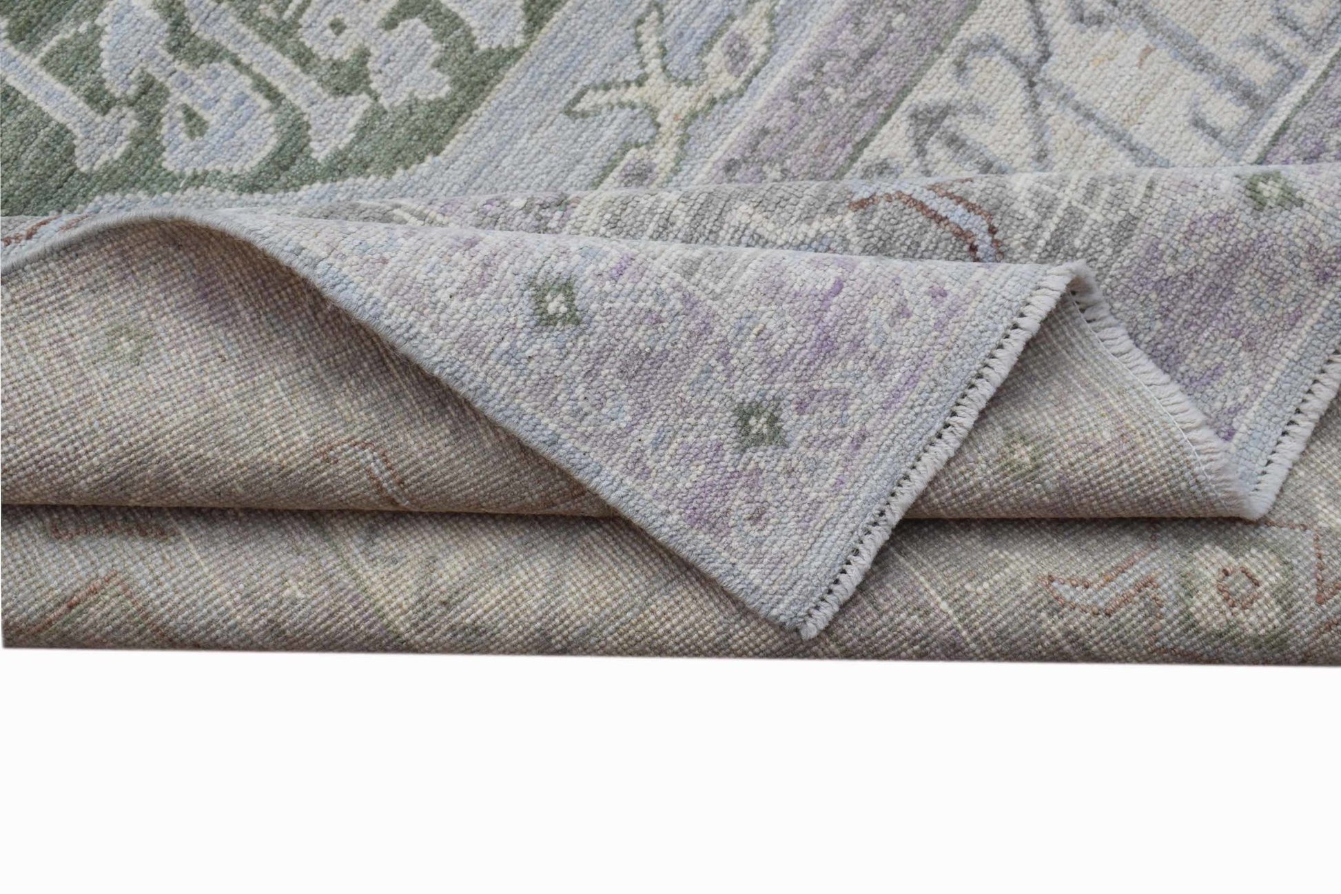 A handwoven transitional Oushak rug featuring a floral pattern in soft green and purple tones.
