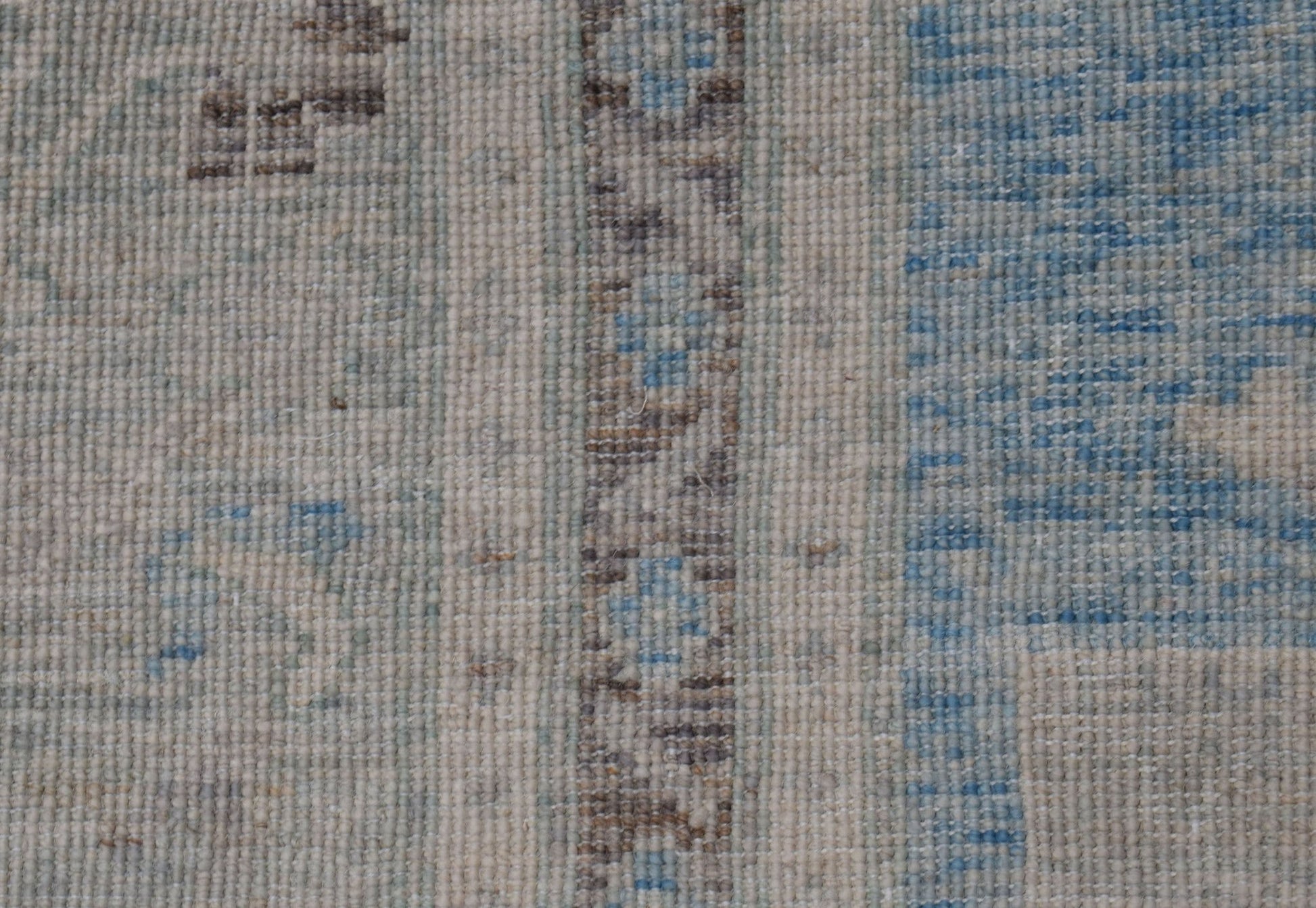 A close-up of a handwoven wool rug featuring a transitional pattern in blue, beige, and brown.