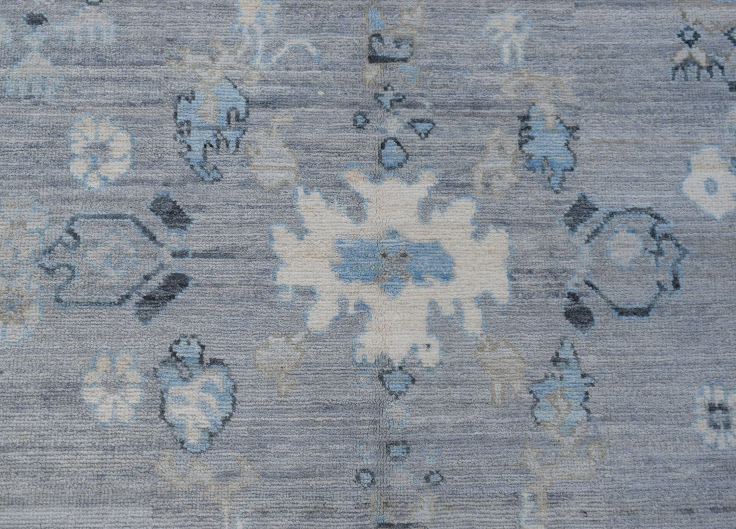 A transitional Oushak rug featuring a floral pattern in shades of blue, grey, and cream.
