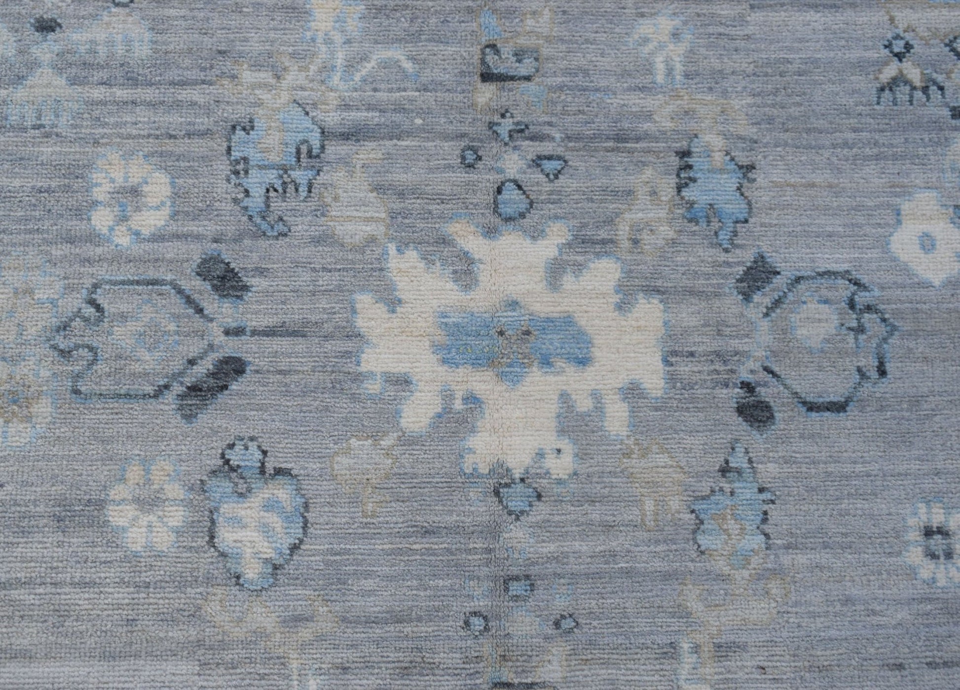 A transitional Oushak rug featuring a floral pattern in shades of blue, grey, and cream.