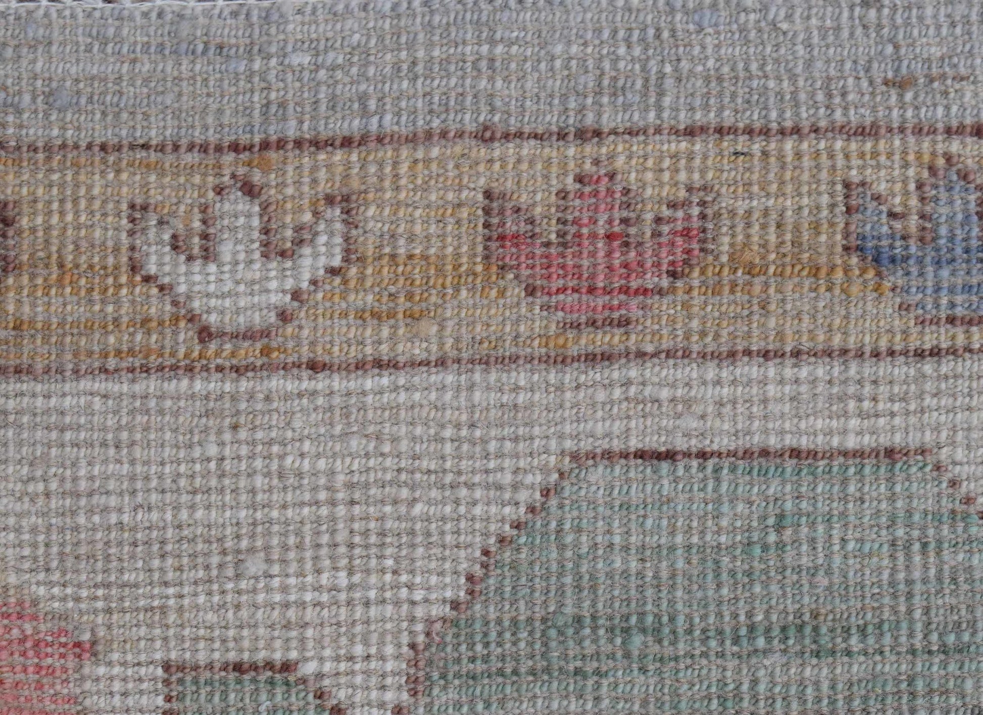 A close-up of a handwoven wool rug featuring a floral border pattern in muted tones.