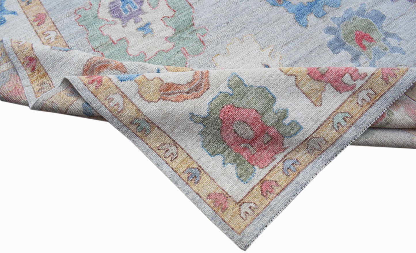 A handwoven transitional Oushak rug featuring a light blue field with colorful floral motifs.