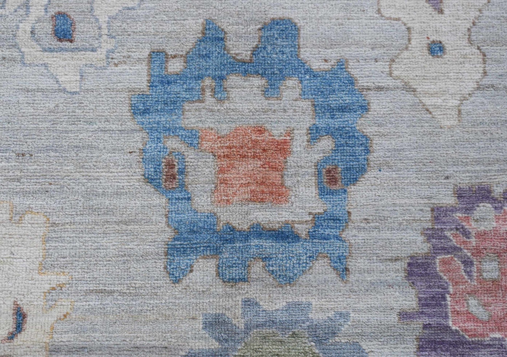 A handwoven transitional Oushak rug featuring a blue floral motif on a light grey wool background.
