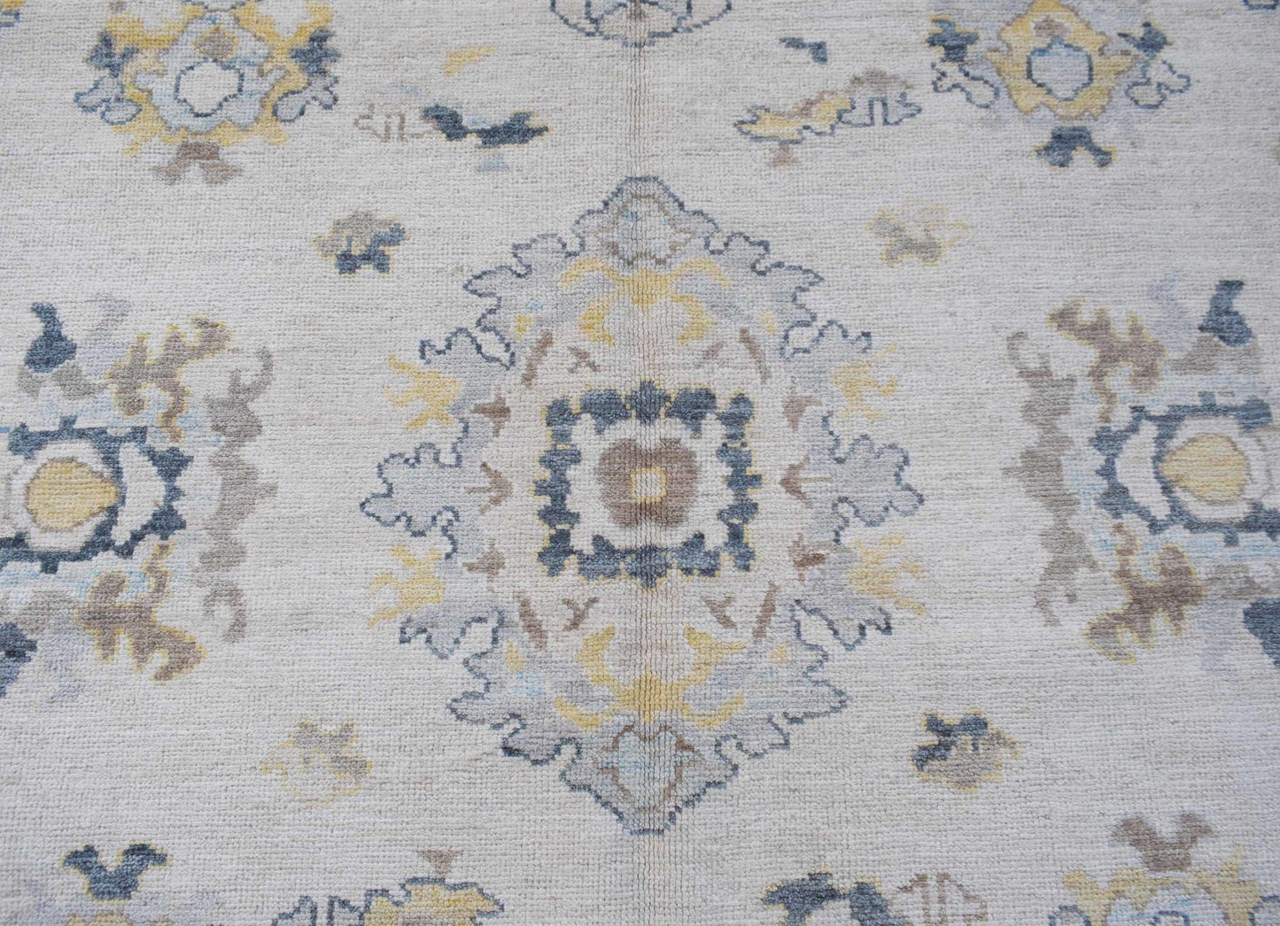 A handwoven transitional Oushak rug featuring a floral pattern in soft blue, yellow, and grey.
