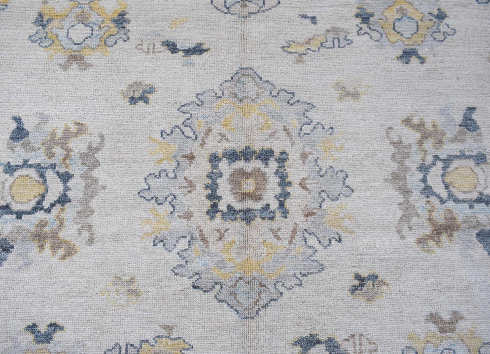 A handwoven transitional Oushak rug featuring a floral pattern in soft blue, yellow, and grey.
