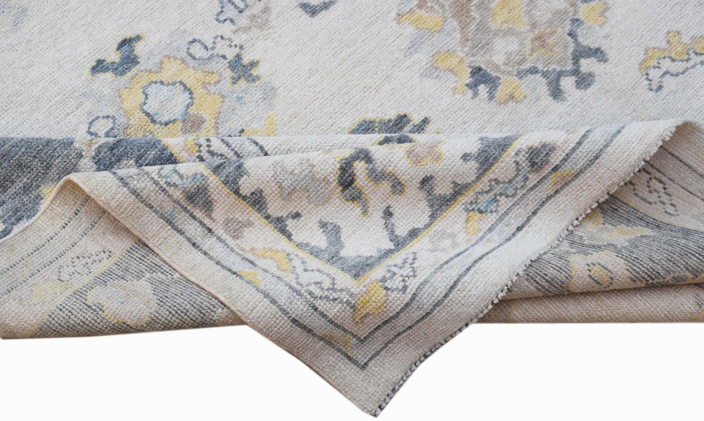 A handwoven transitional Oushak rug featuring a floral pattern in grey, yellow, and cream tones.