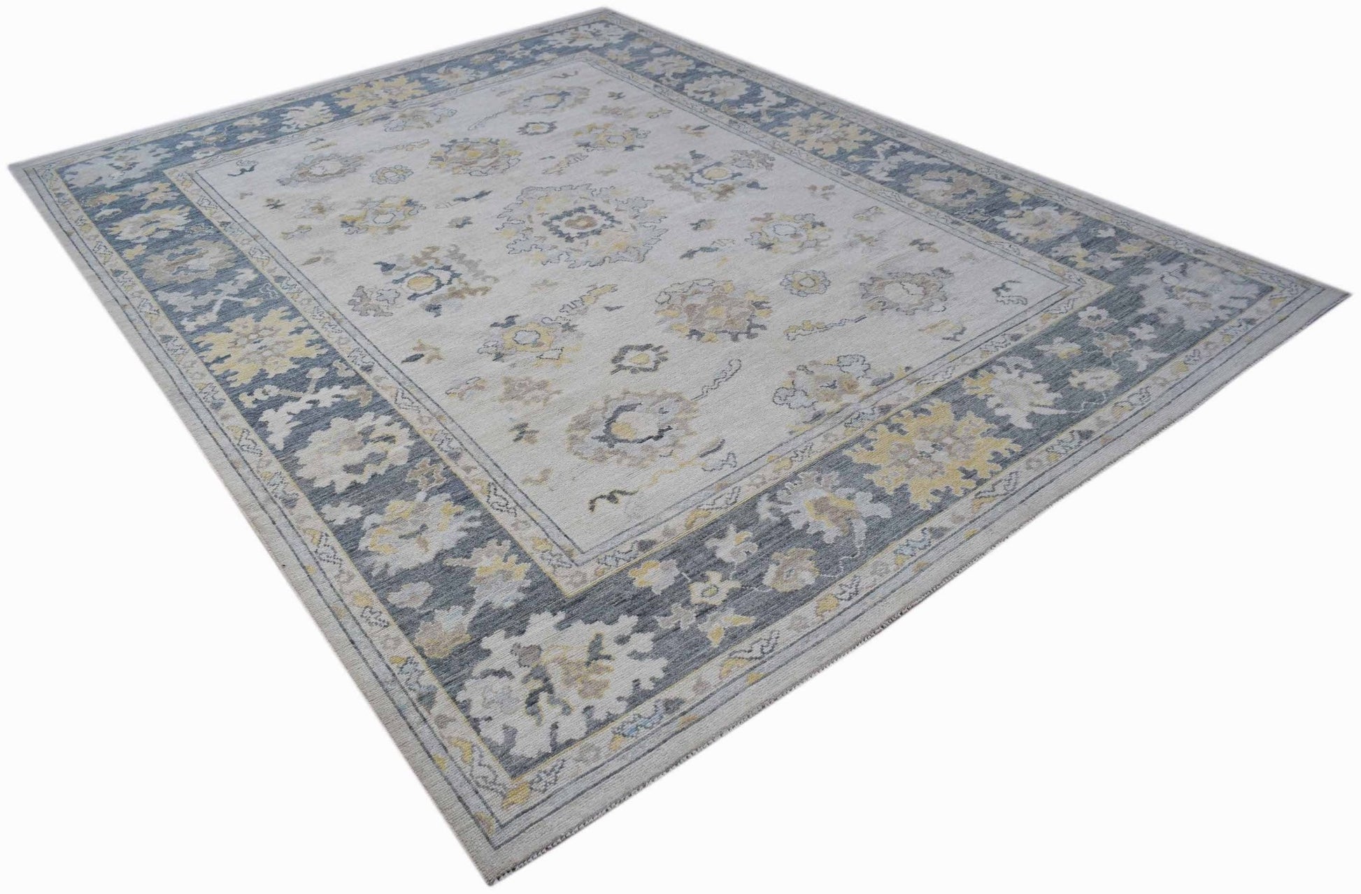 A handwoven transitional Oushak rug featuring a floral pattern in blue, grey, and yellow tones.