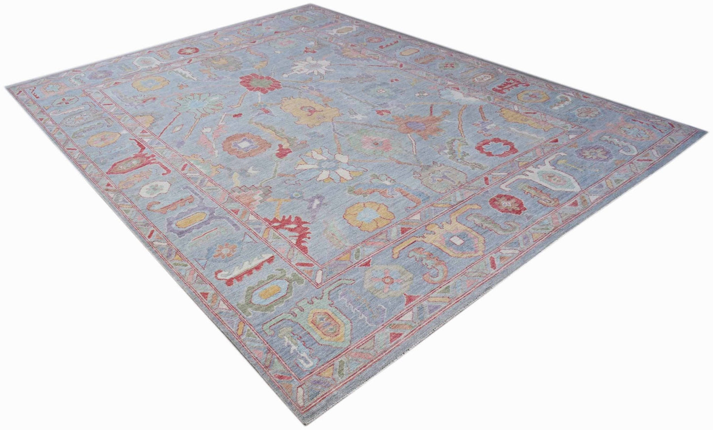 A handwoven transitional Oushak rug featuring a floral pattern in soft blue and multi-colored tones.