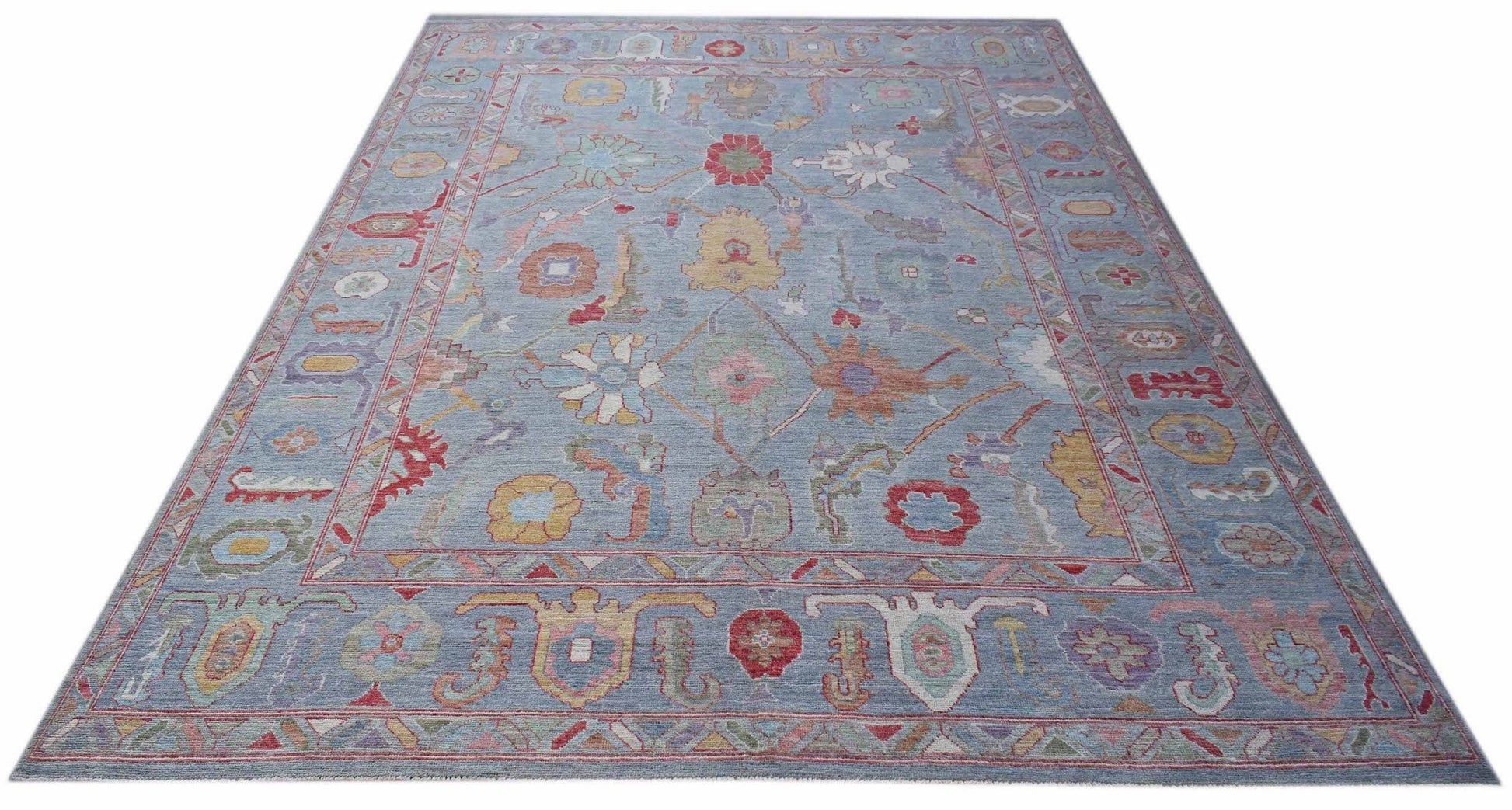 A handwoven transitional Oushak rug featuring a floral pattern in soft colors on a blue background.