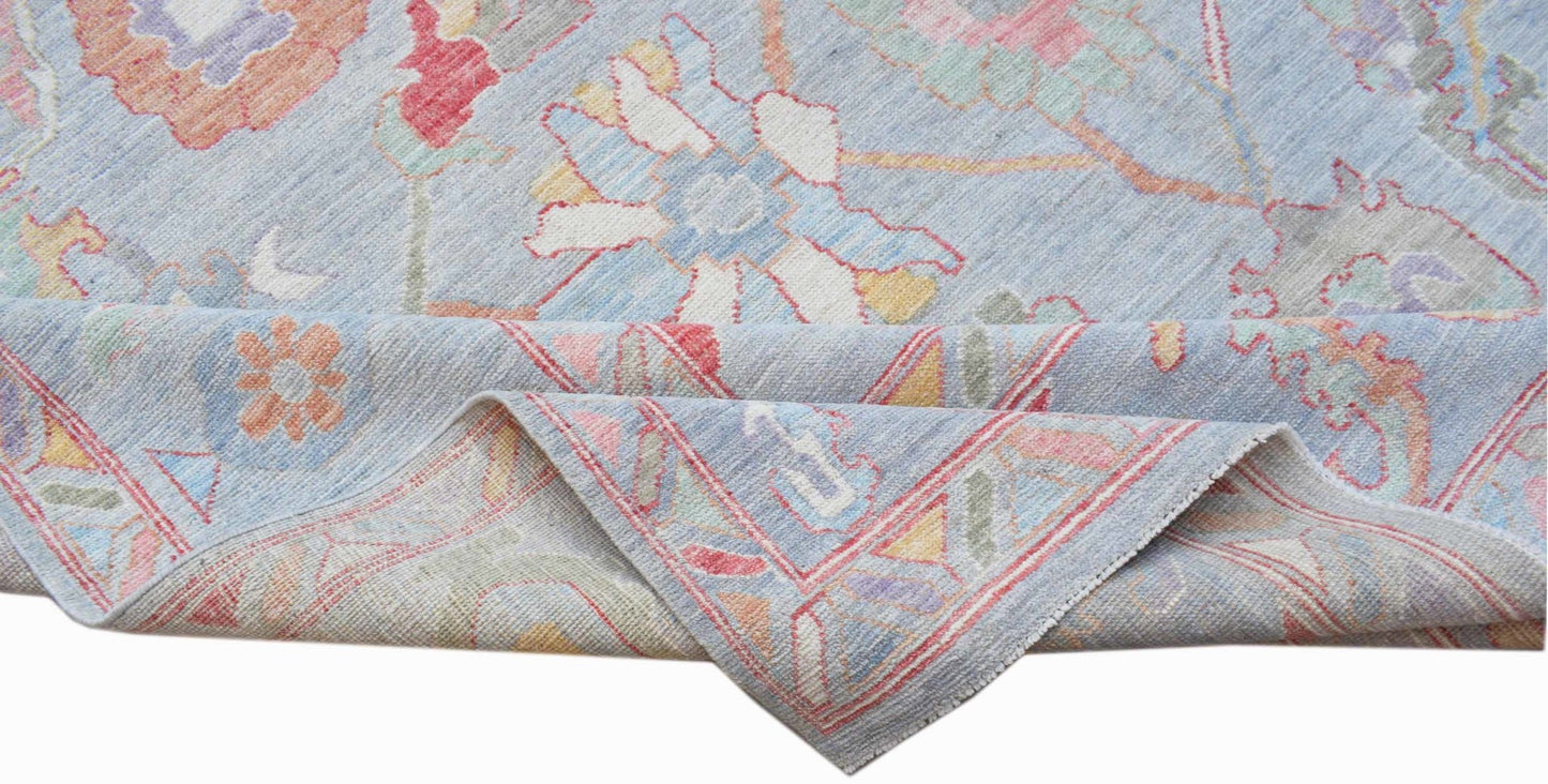 A handwoven transitional Oushak rug featuring a floral pattern in soft pastel colors on blue.