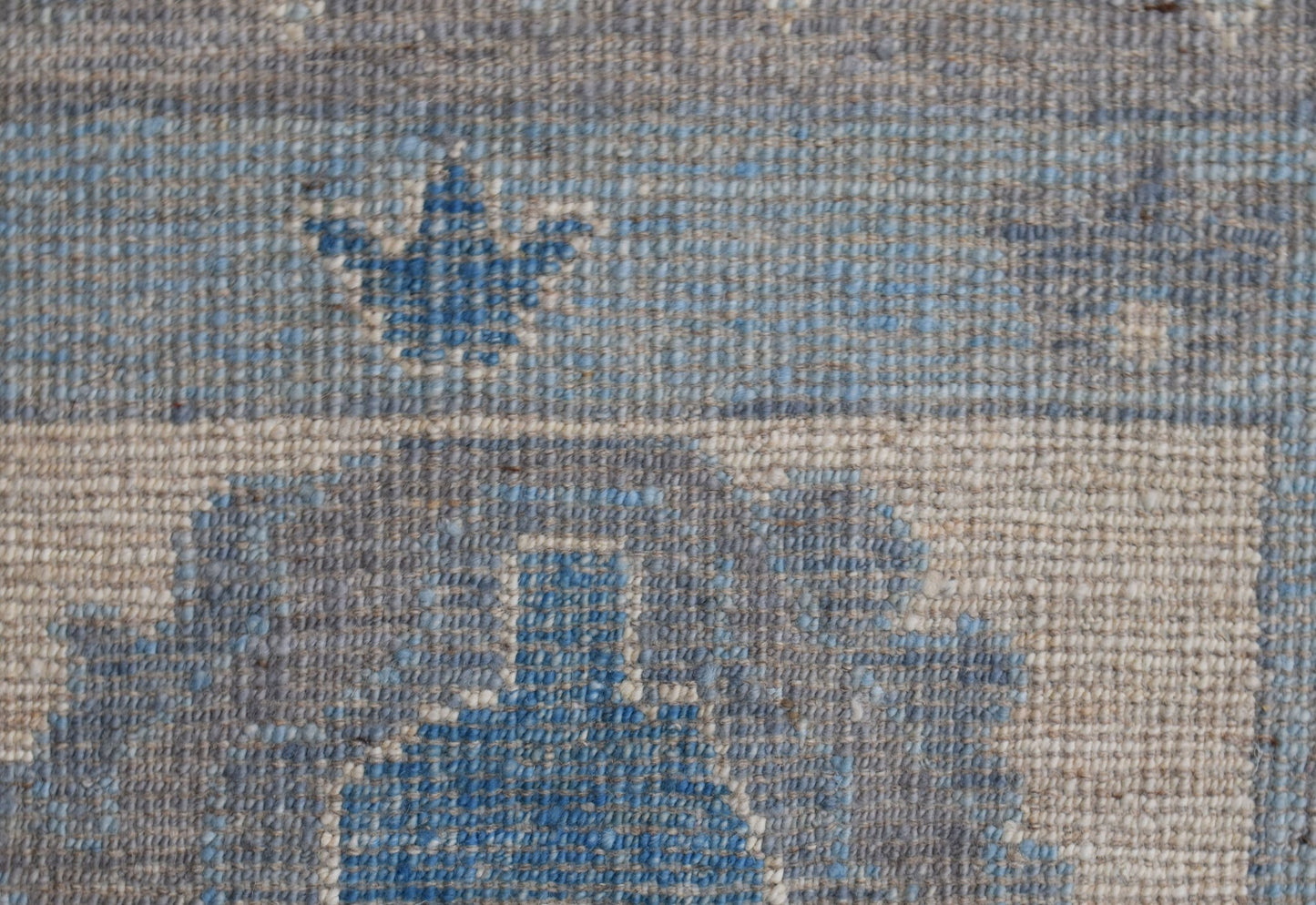 A close-up of a handwoven wool rug featuring a blue floral motif on a textured beige background.