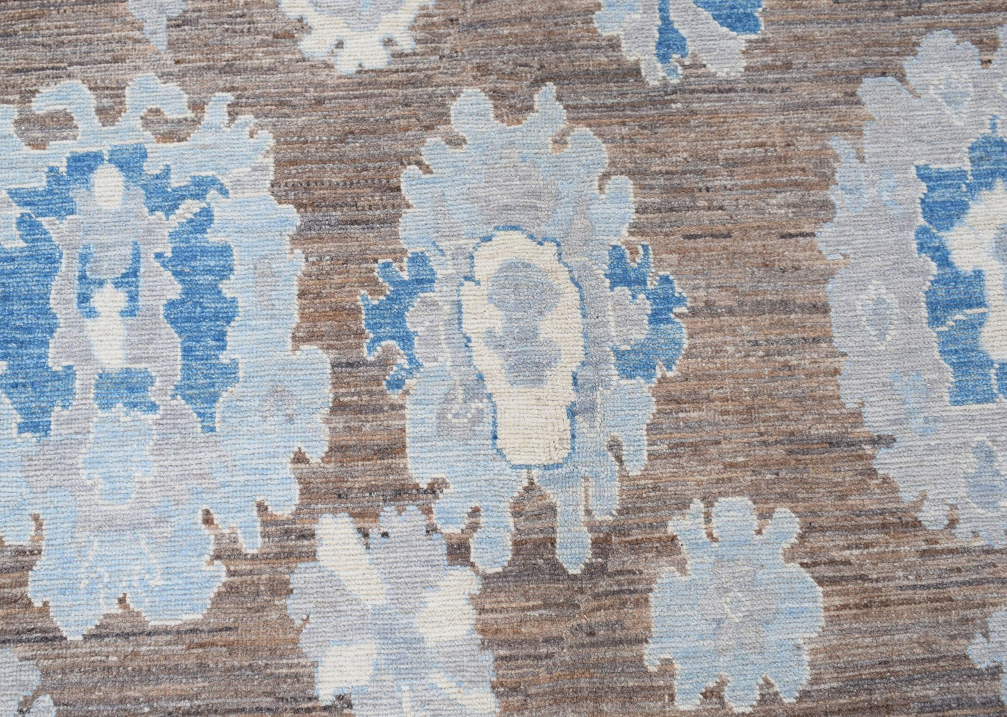 A transitional Oushak rug featuring a blue and cream floral pattern on a textured brown background.