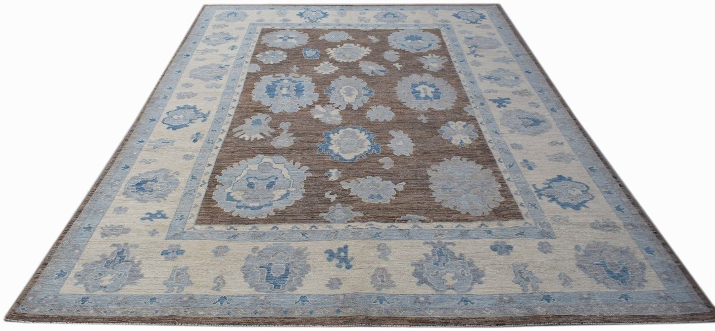 A handwoven transitional Oushak rug featuring a brown field with blue floral motifs and a wide border.