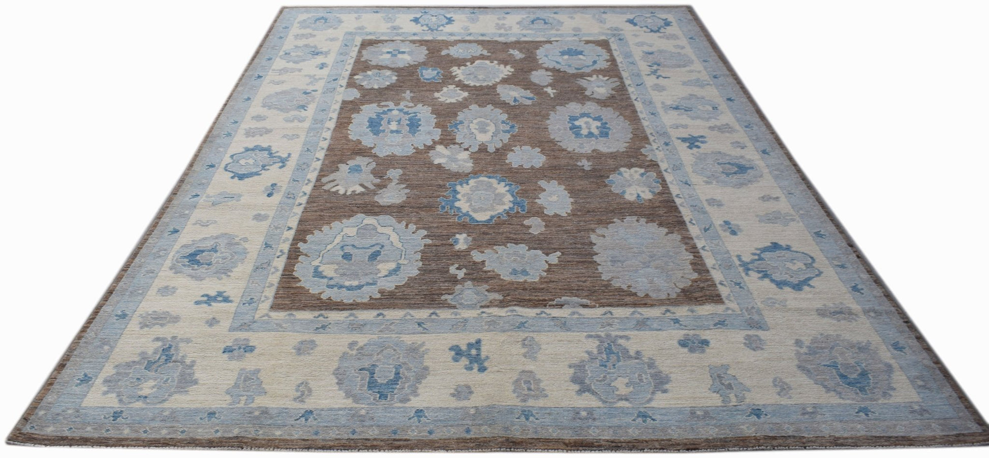 A handwoven transitional Oushak rug featuring a brown field with blue floral motifs and a wide border.