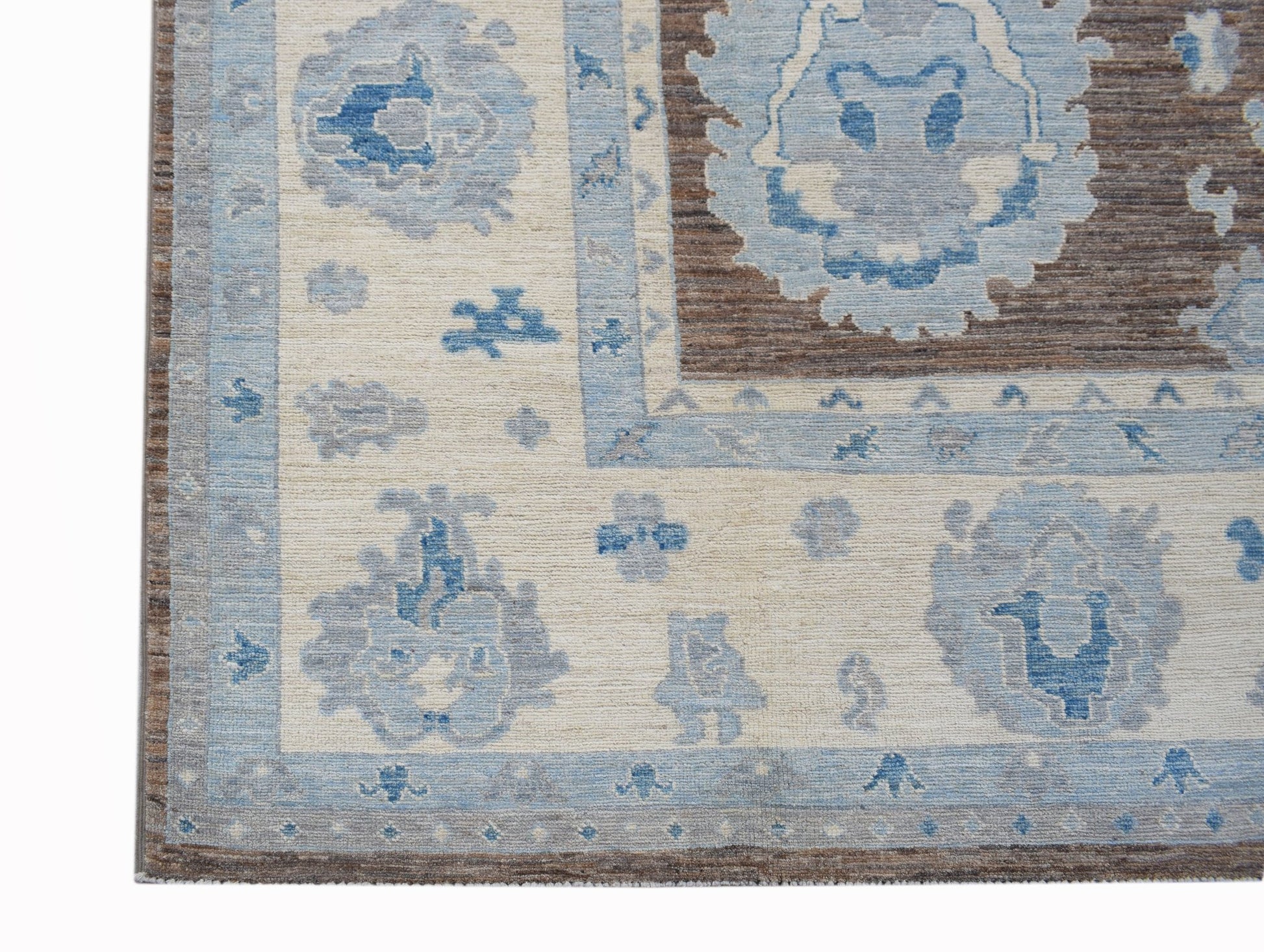 A handwoven transitional Oushak rug featuring a floral pattern in shades of blue, cream, and brown.