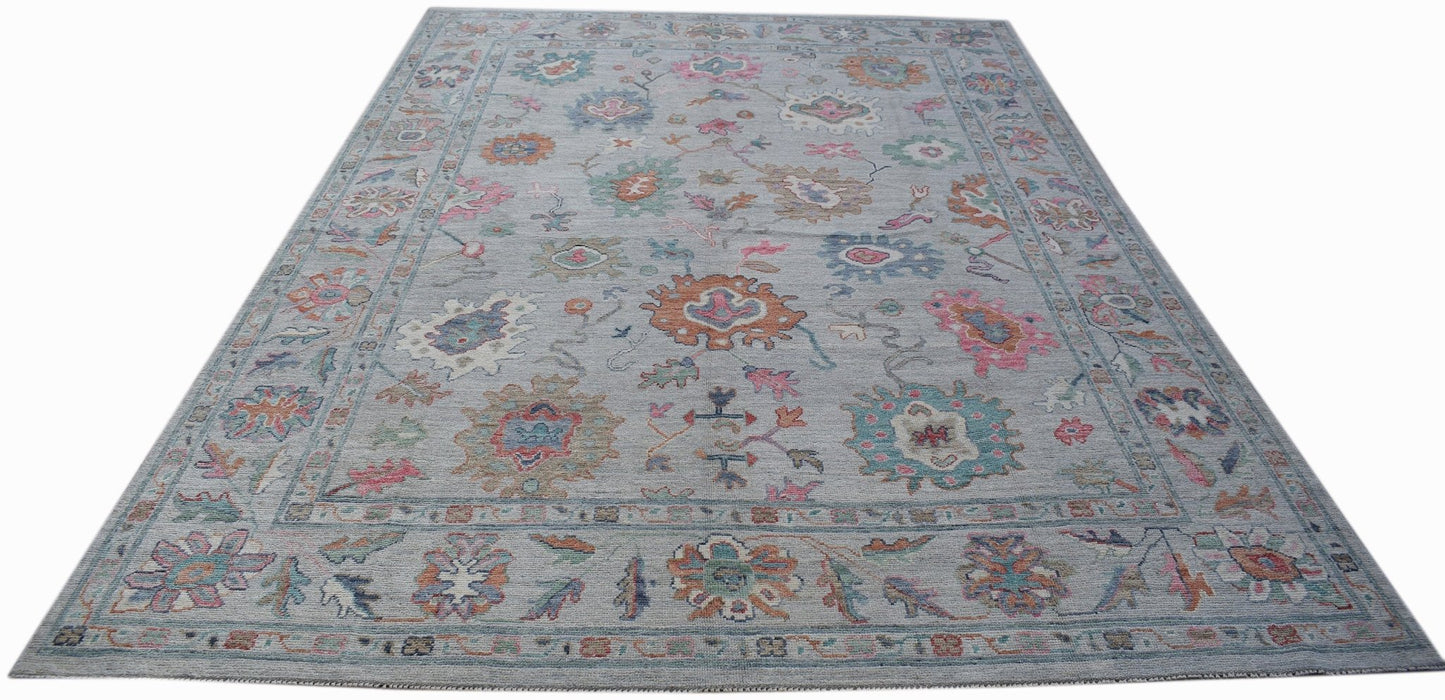 A handwoven transitional Oushak rug featuring a floral pattern in soft colors on a grey background.