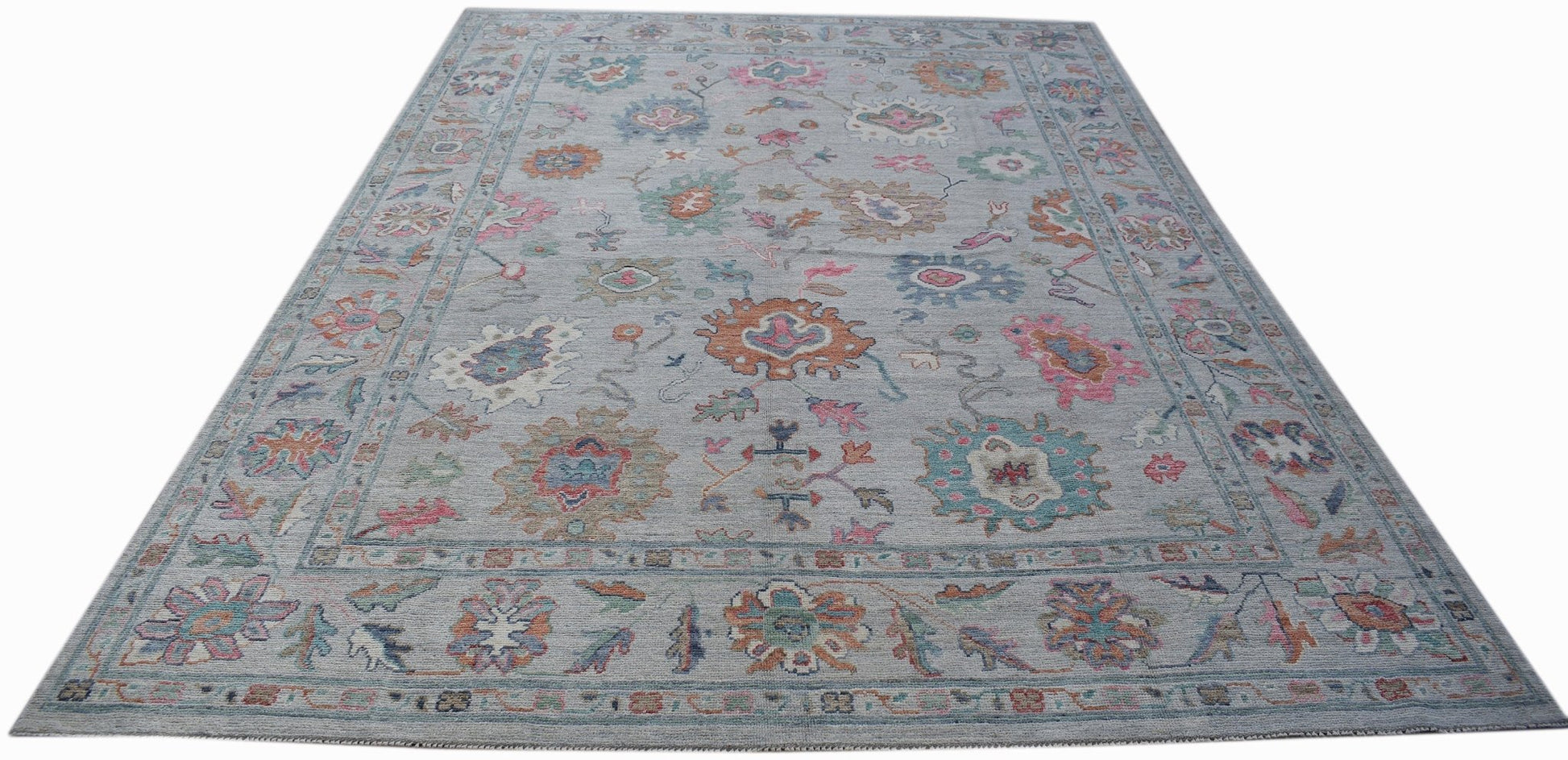A handwoven transitional Oushak rug featuring a floral pattern in soft colors on a grey background.