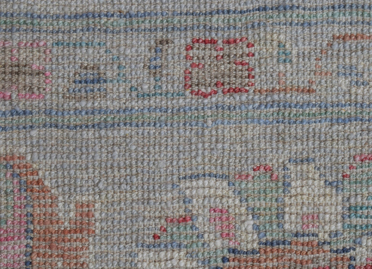 A close-up of a handwoven wool rug featuring a transitional pattern in soft, muted tones.