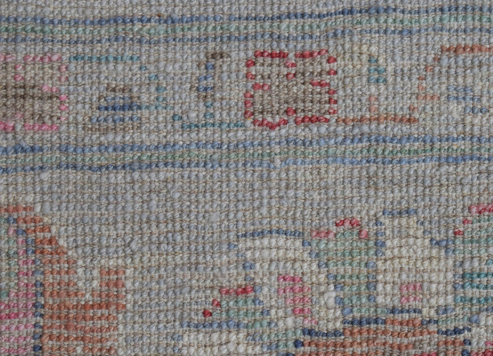 A close-up of a handwoven wool rug featuring a transitional pattern in soft, muted tones.