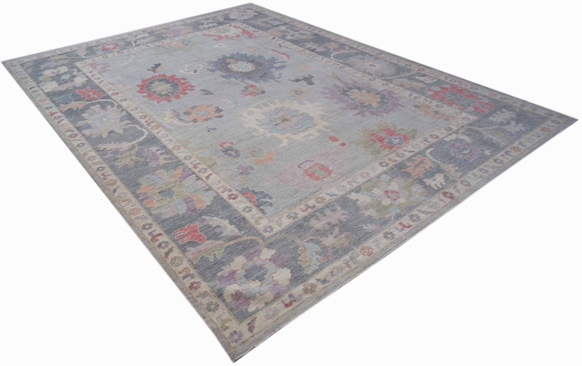 A handwoven transitional Oushak rug featuring a floral pattern in muted tones on a grey field.