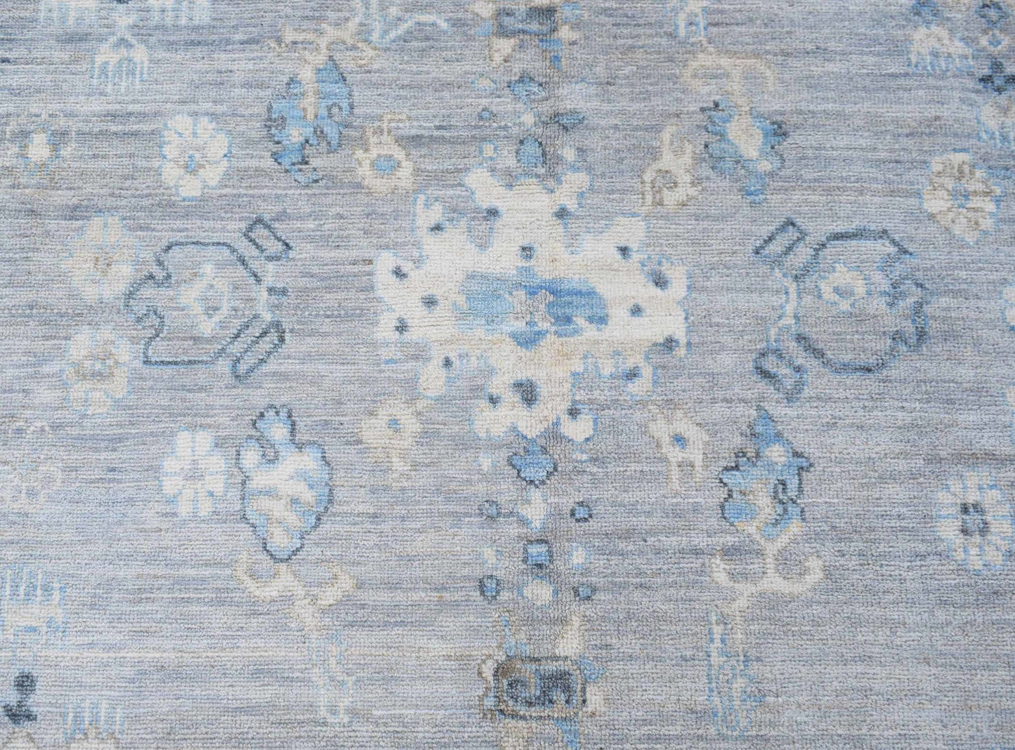 A handwoven transitional Oushak rug featuring a floral pattern in shades of blue and cream.