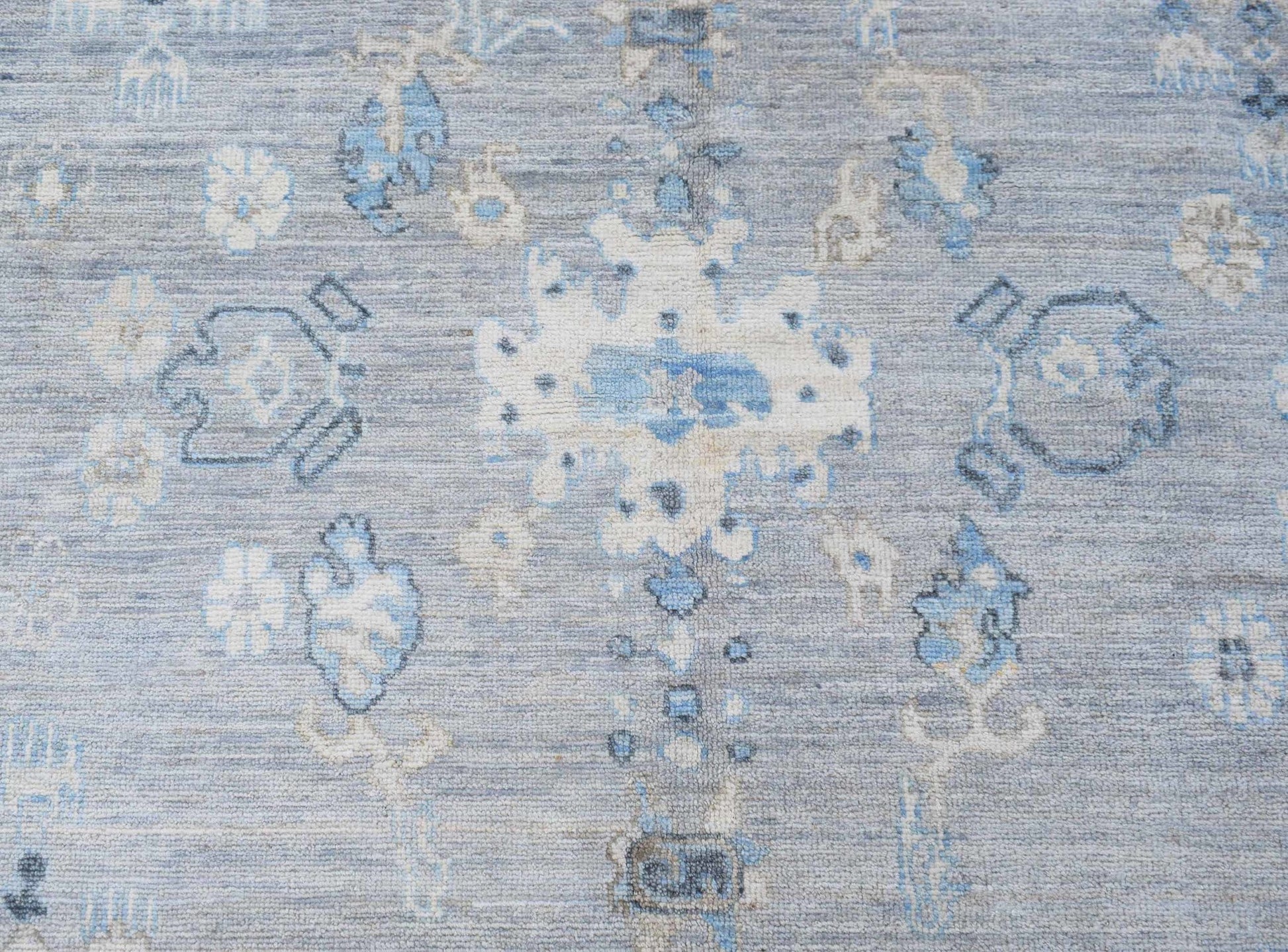 A handwoven transitional Oushak rug featuring a floral pattern in shades of blue and cream.