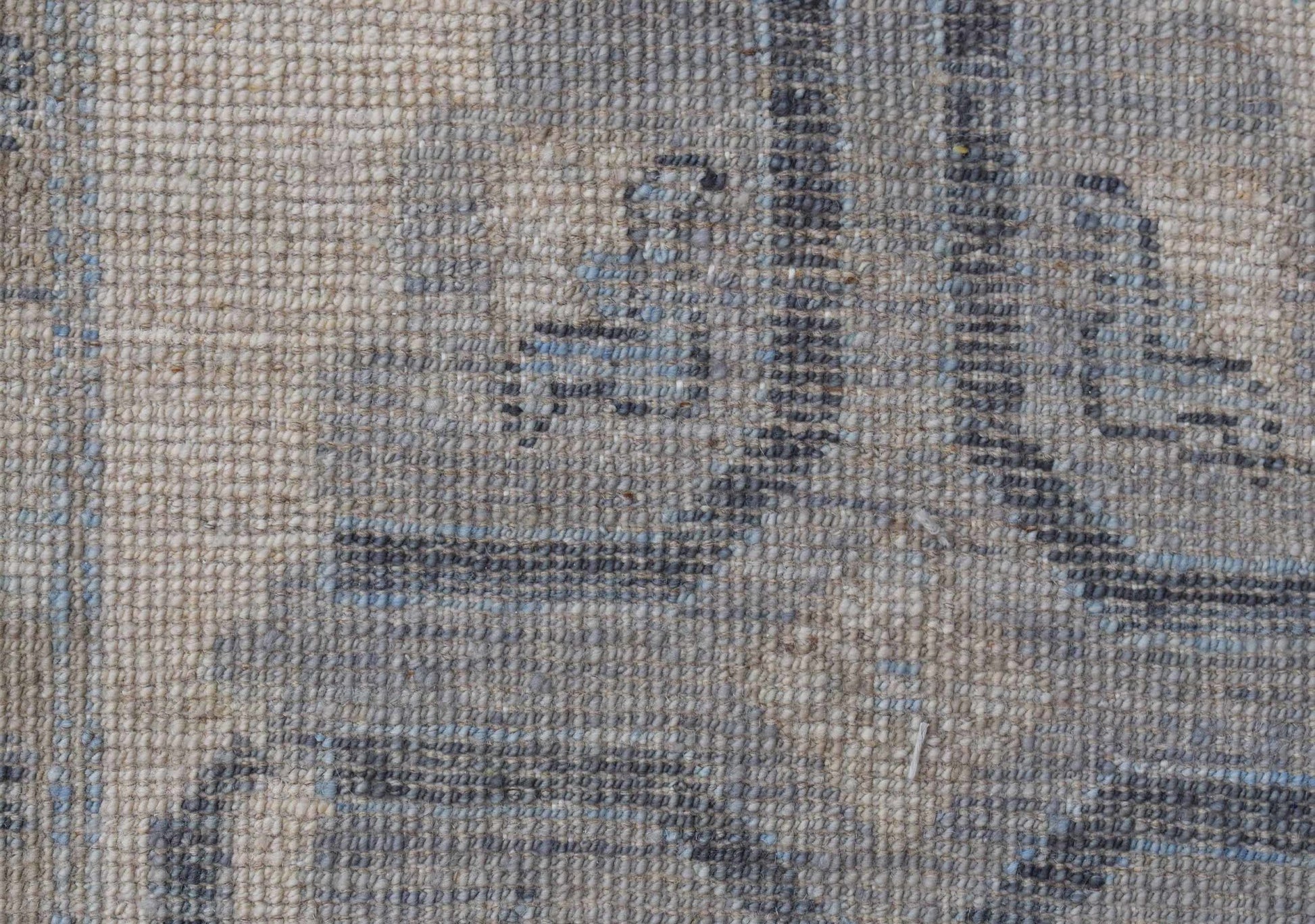 A close-up view of a handwoven wool rug featuring a faded blue and beige floral pattern.