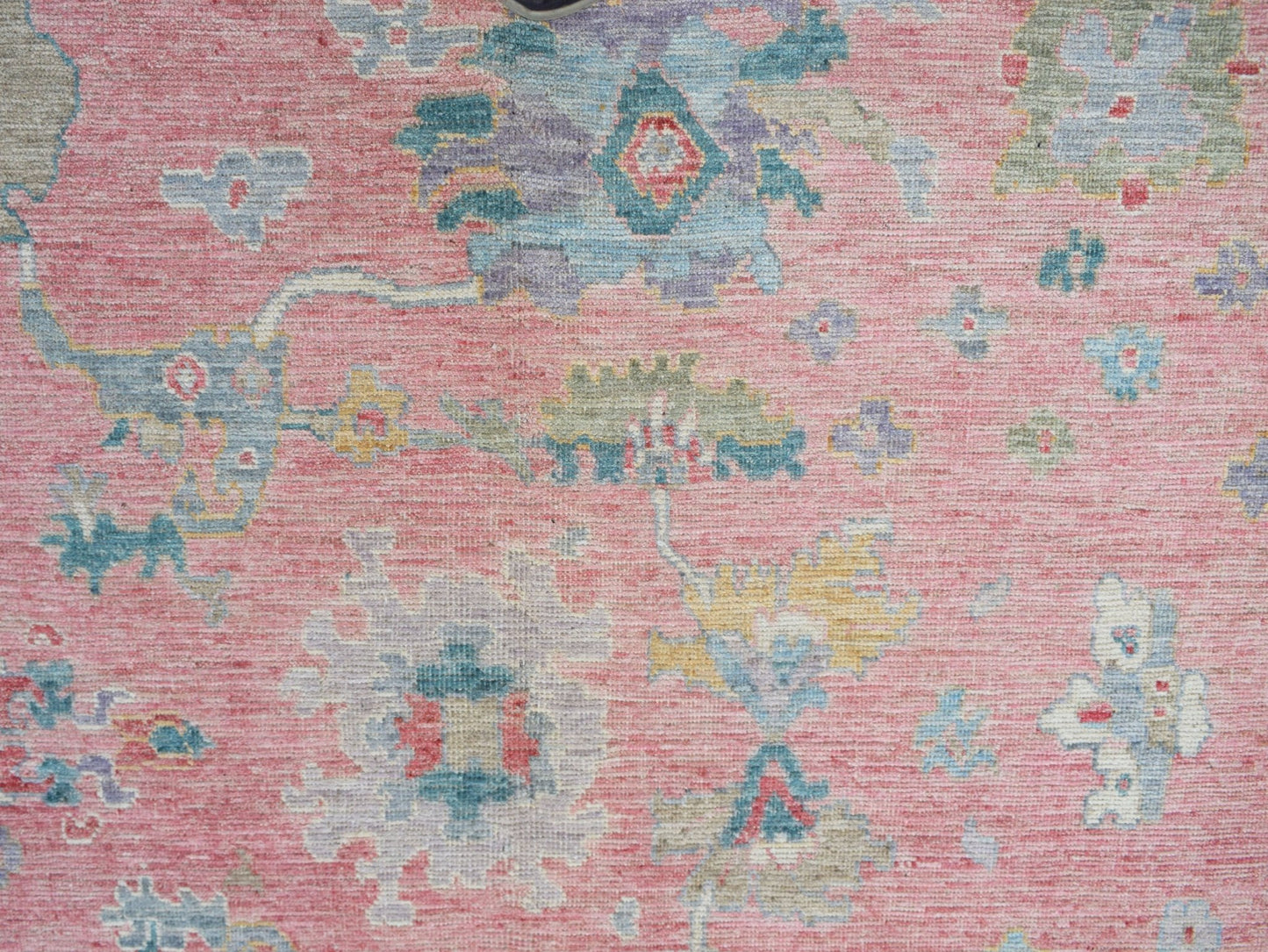 A handwoven transitional Oushak rug featuring a floral pattern in muted tones on a pink background.