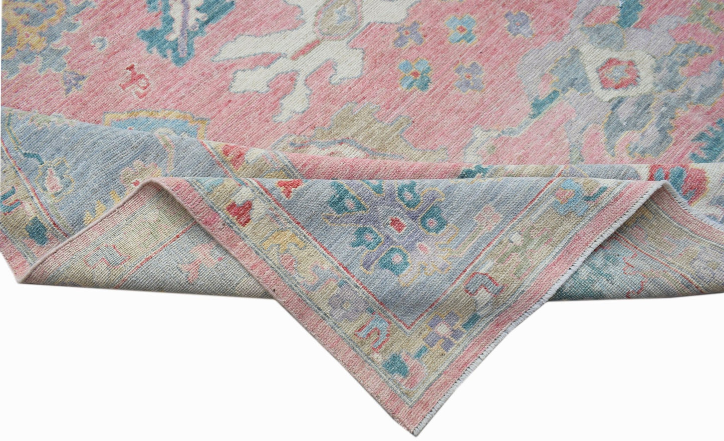 A handwoven transitional Oushak rug featuring a floral pattern in pink, blue, and neutral tones.