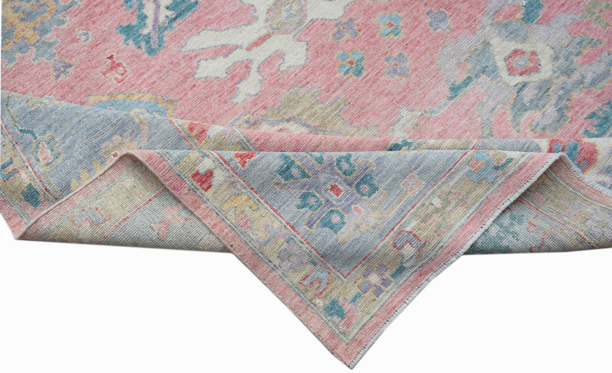 A handwoven transitional Oushak rug featuring a floral pattern in pink, blue, and neutral tones.