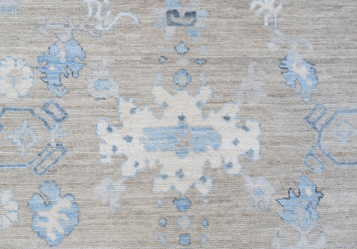 A handwoven transitional Oushak rug featuring a light blue and white floral pattern on a beige base.
