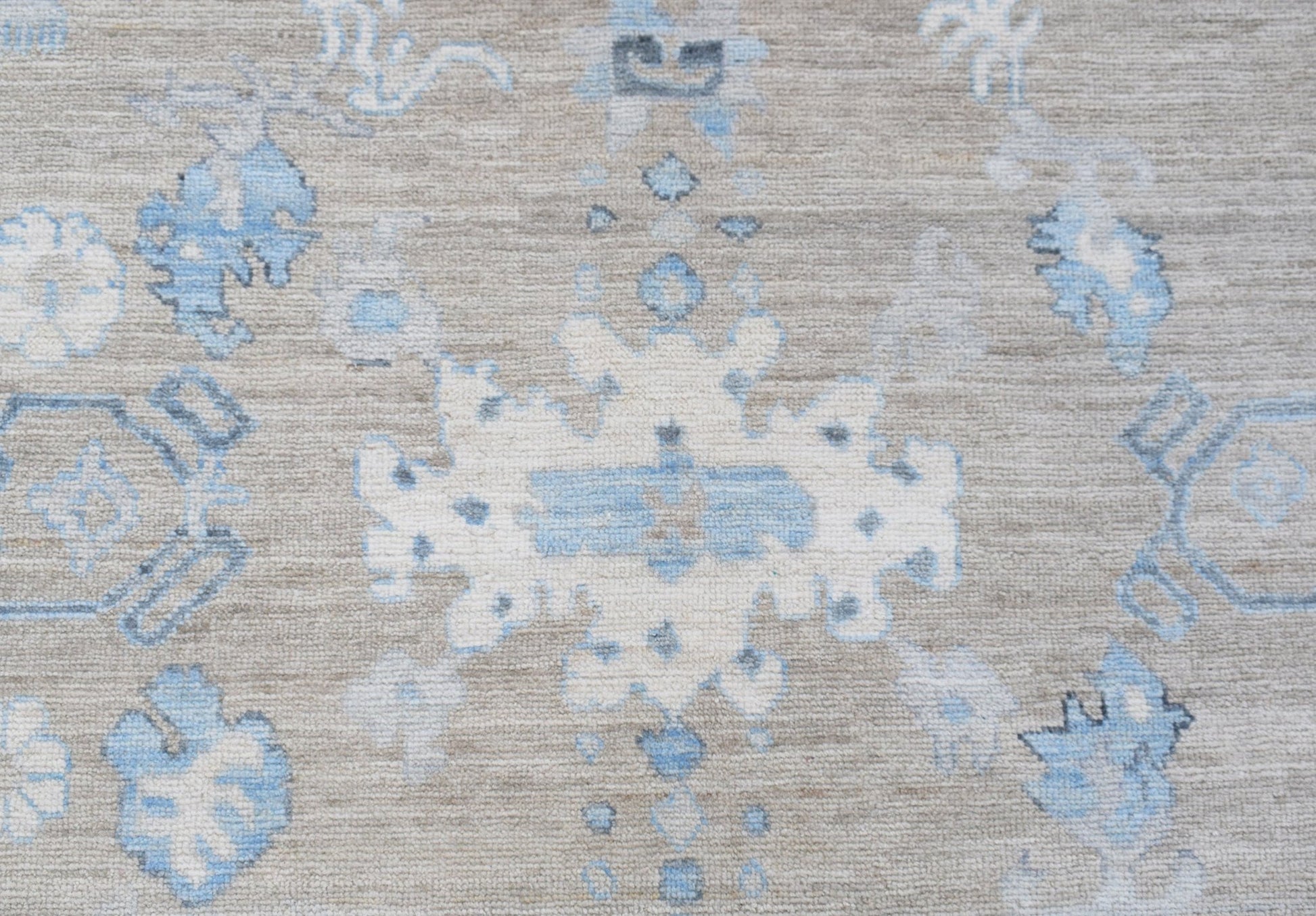 A handwoven transitional Oushak rug featuring a light blue and white floral pattern on a beige base.