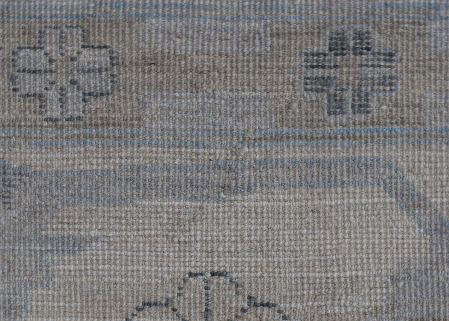 A close-up of a handwoven wool rug featuring a neutral beige background with subtle blue linear accents and geometric motifs.