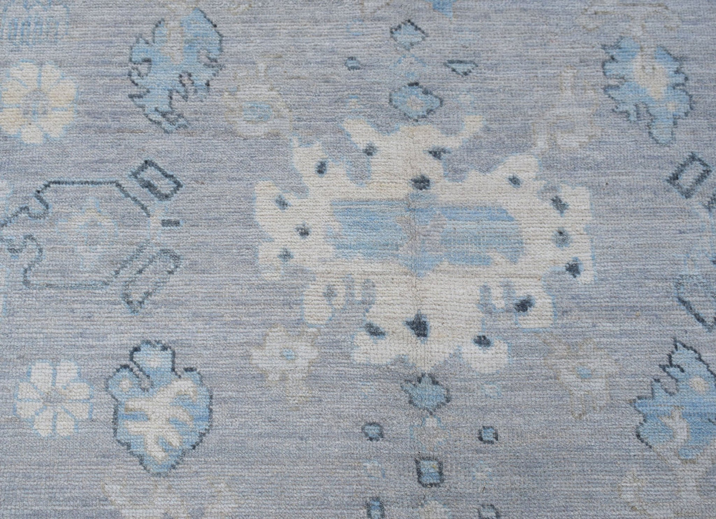 A transitional Oushak rug featuring a light blue field with cream and grey floral motifs.