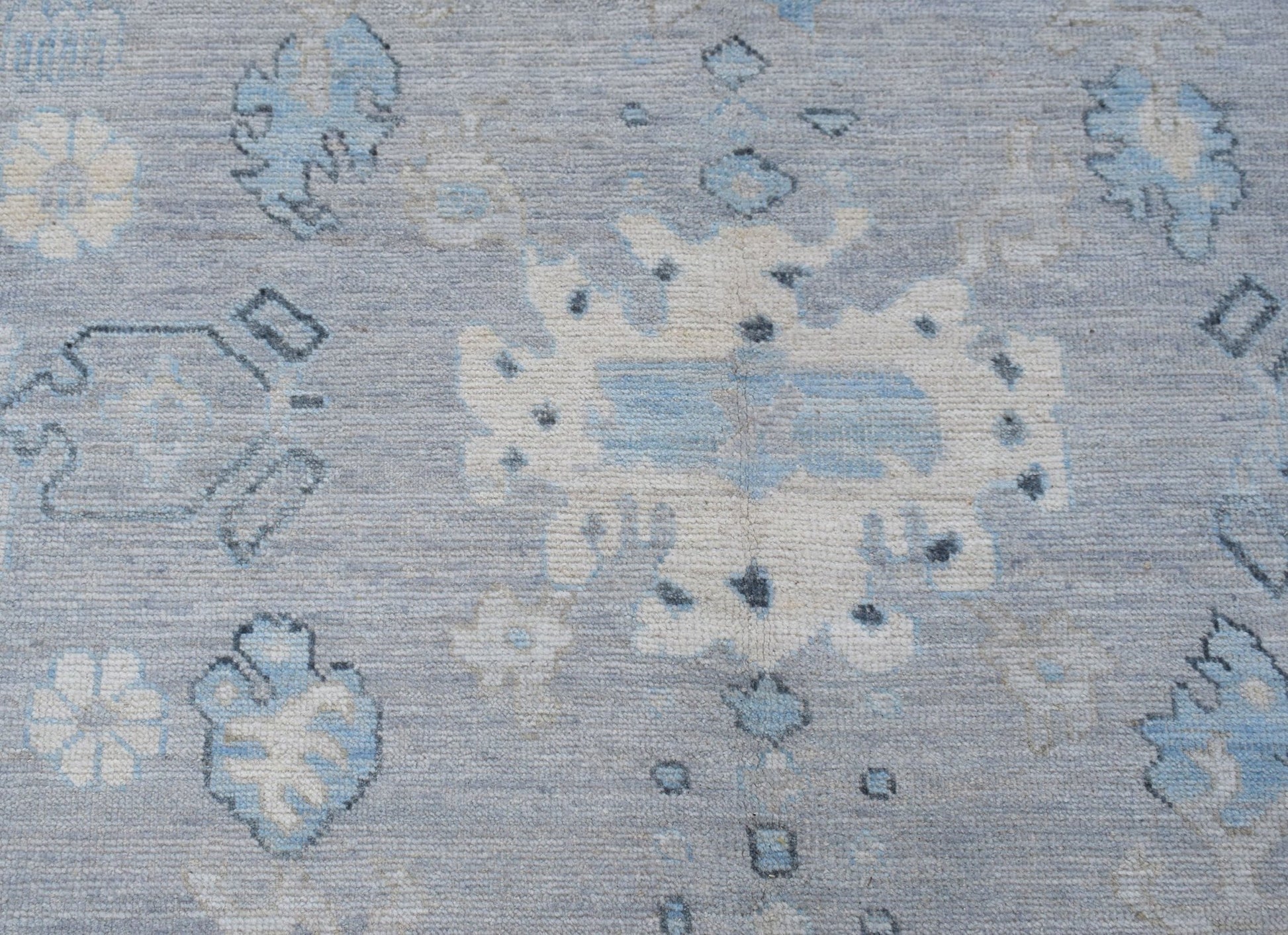A transitional Oushak rug featuring a light blue field with cream and grey floral motifs.
