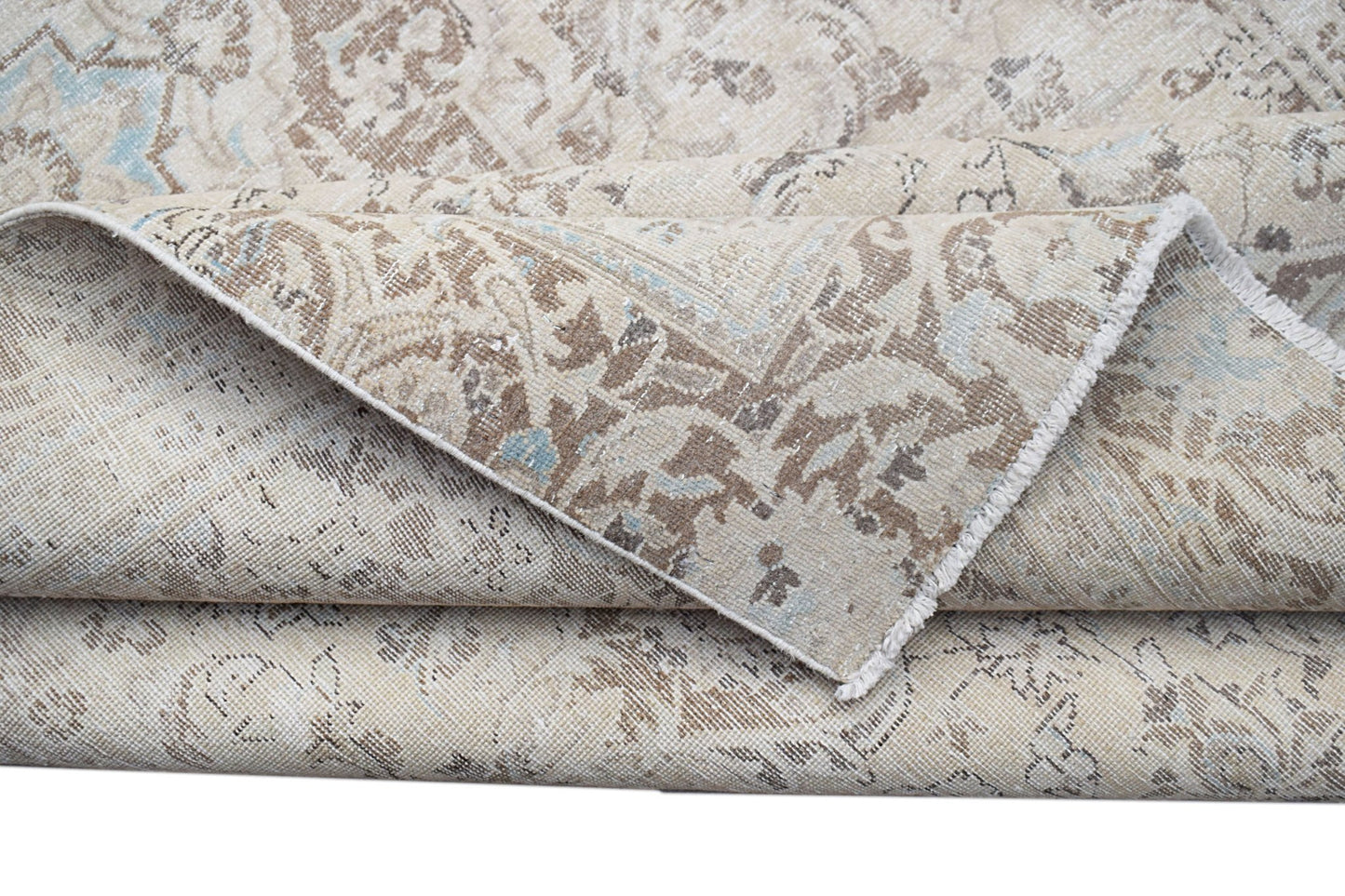 A folded vintage Persian Kerman rug featuring a neutral palette with intricate floral patterns.
