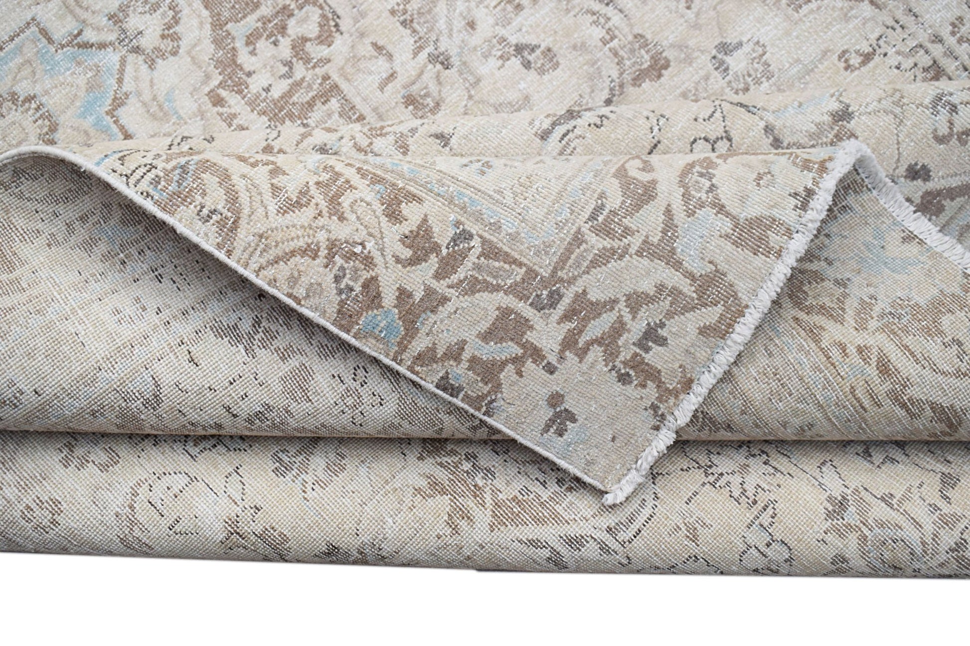 A folded vintage Persian Kerman rug featuring a neutral palette with intricate floral patterns.