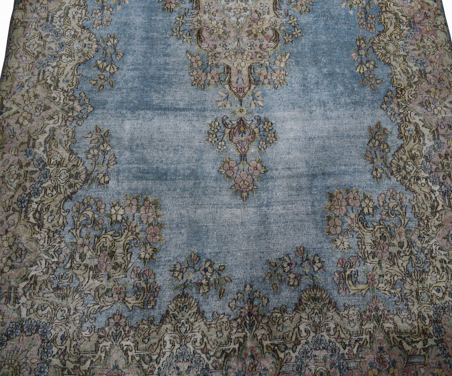 A vintage Persian Kerman rug featuring a blue field with intricate floral patterns and a medallion.